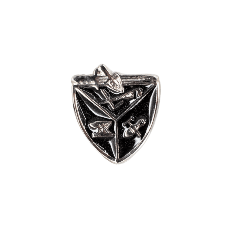A small shield-shaped silver-toned emblem or charm with black recessed sections and engraved symbols, centered on a plain white background.