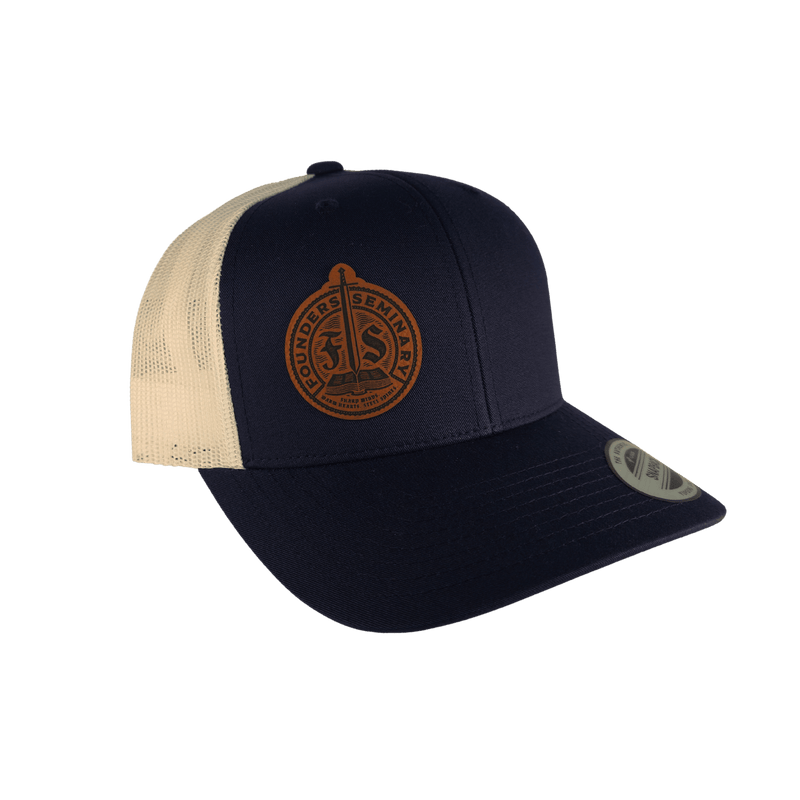 A navy blue and cream trucker hat with a circular brown embroidered patch on the front panel, shown against a solid green background.