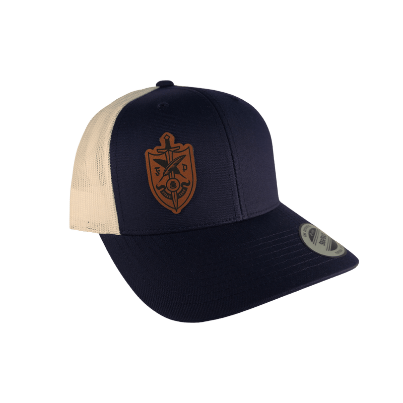 A navy blue and cream trucker cap with a brown shield logo on the front [Blue]
