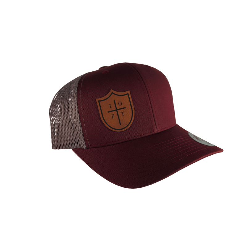 A maroon trucker hat with a brown shield logo on the front, featuring a maroon front panel and brim, and a gray mesh back.