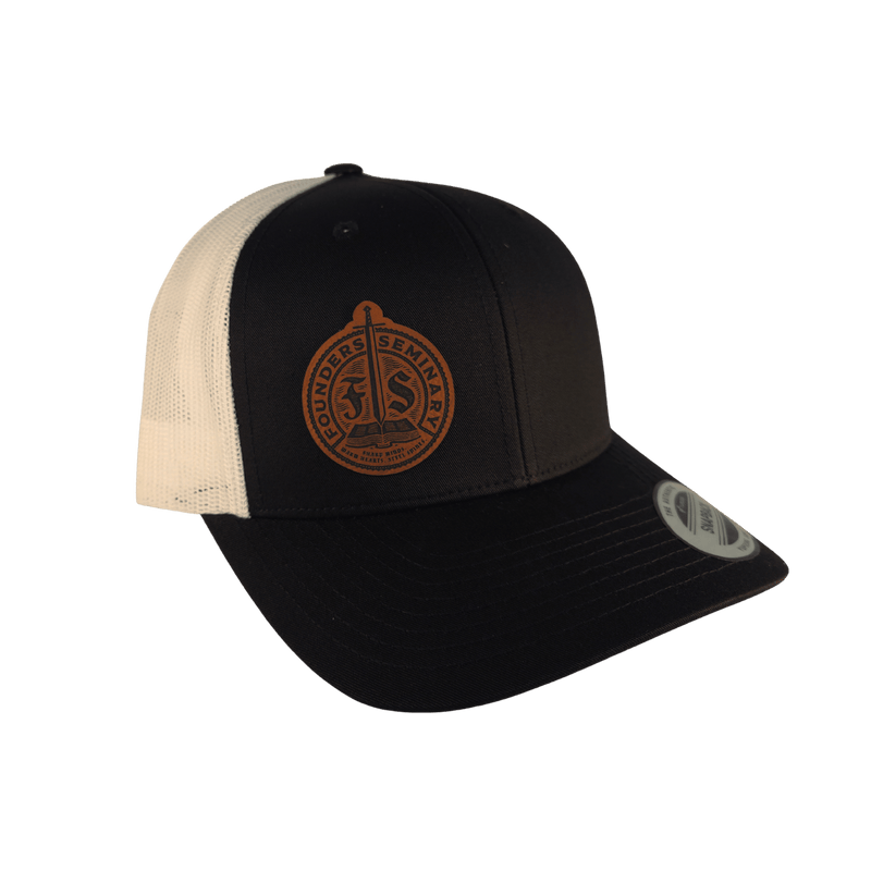 A black and off-white trucker cap with a brown leather patch on the front displaying the 'Founders Seminary' logo.