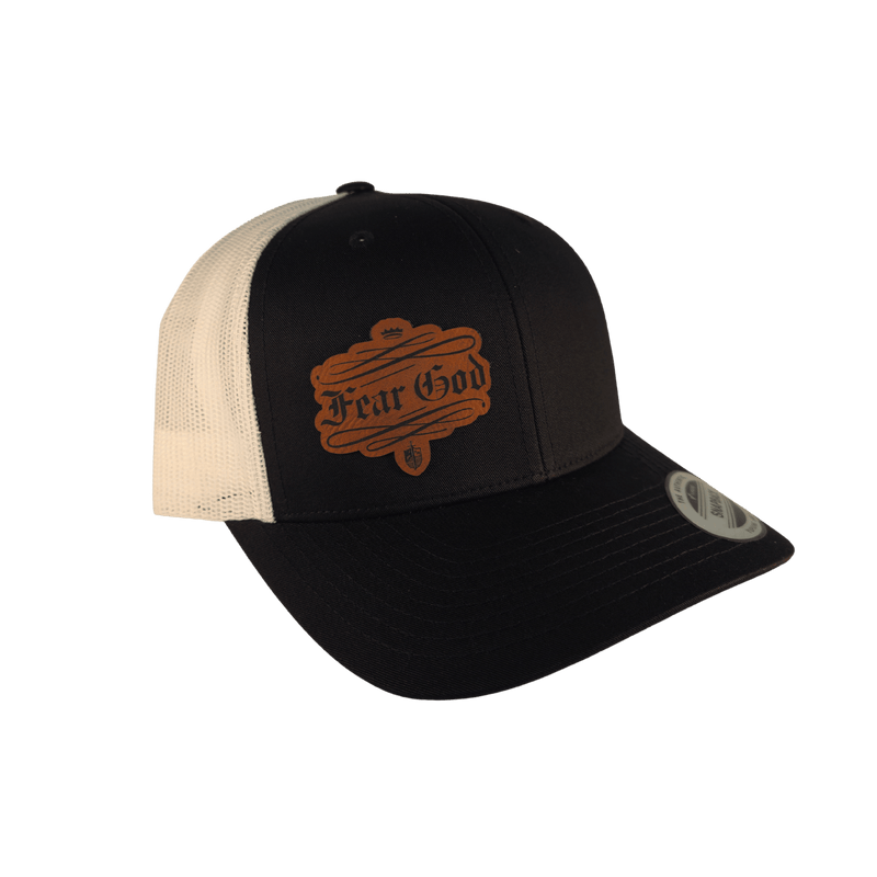 A black and cream trucker hat with a brown faux-leather patch on the front that reads 'Fear God'.