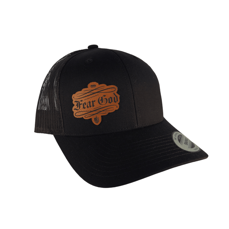 A black trucker-style cap with a brown faux-leather 'Fear God' logo patch on the front panel and a silver New Era sticker on the brim, shown against a plain white background.