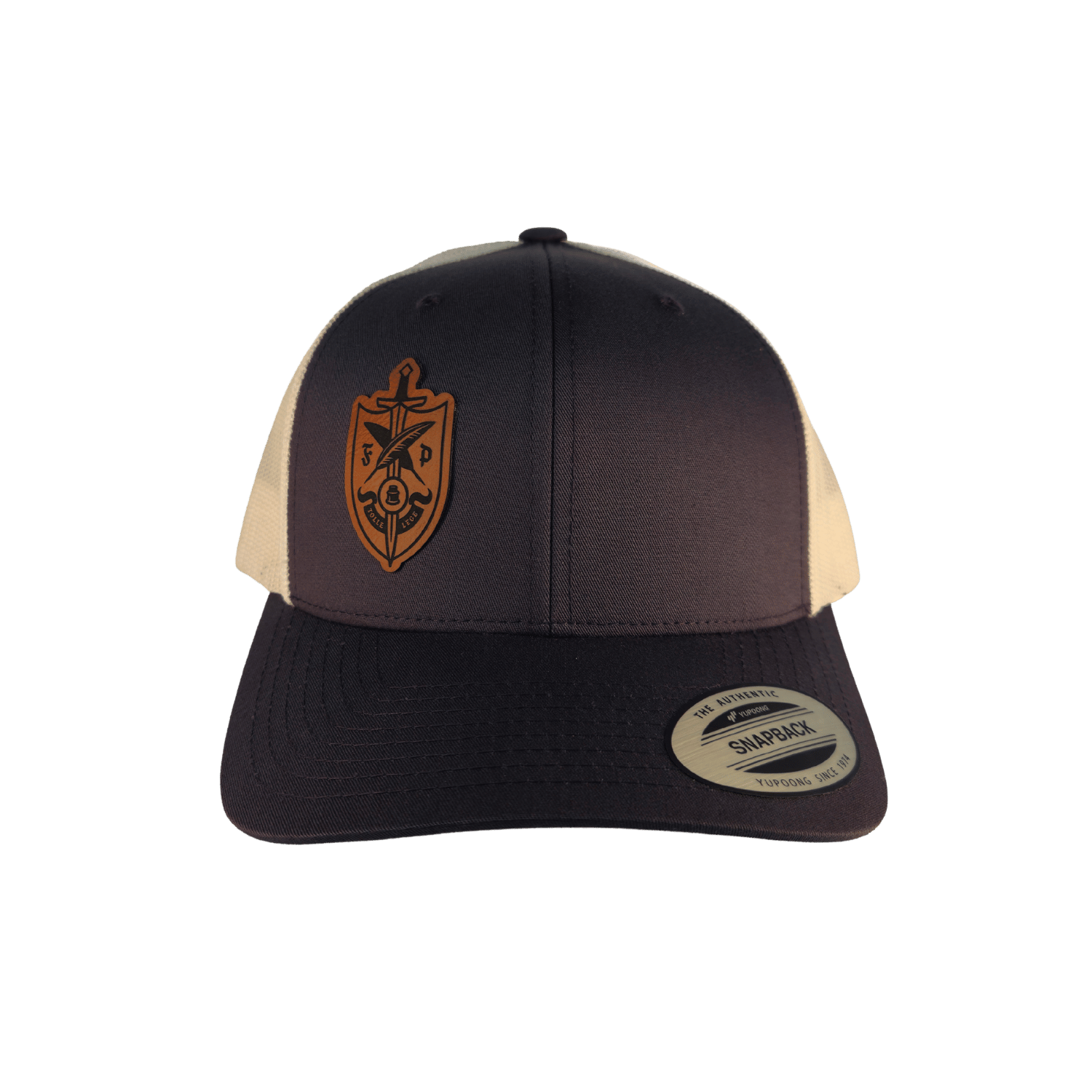 A structured trucker-style baseball cap with a dark grey front and brim, cream mesh side panels, and a brown shield emblem on the front. 