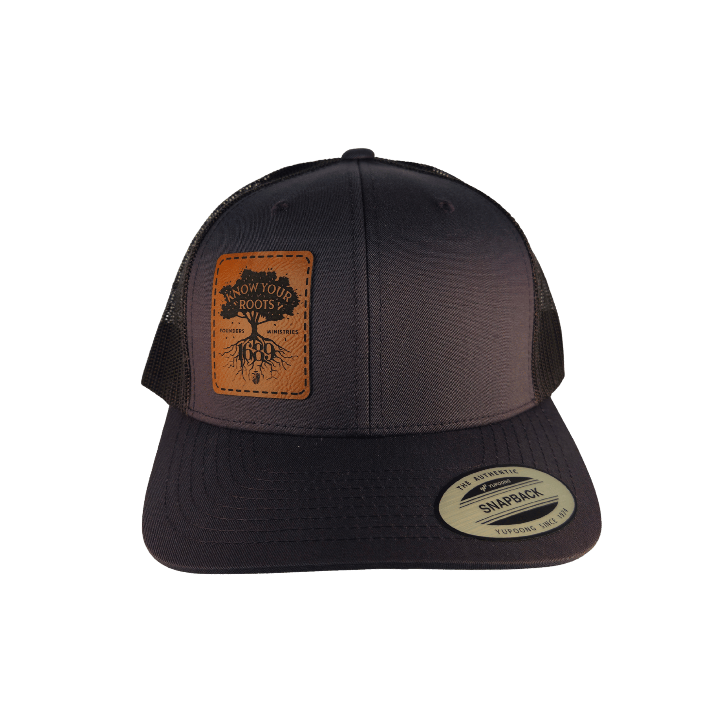 A charcoal trucker hat with a brown leather patch on the front displaying 'Know Your Roots 1689' and a tree graphic.