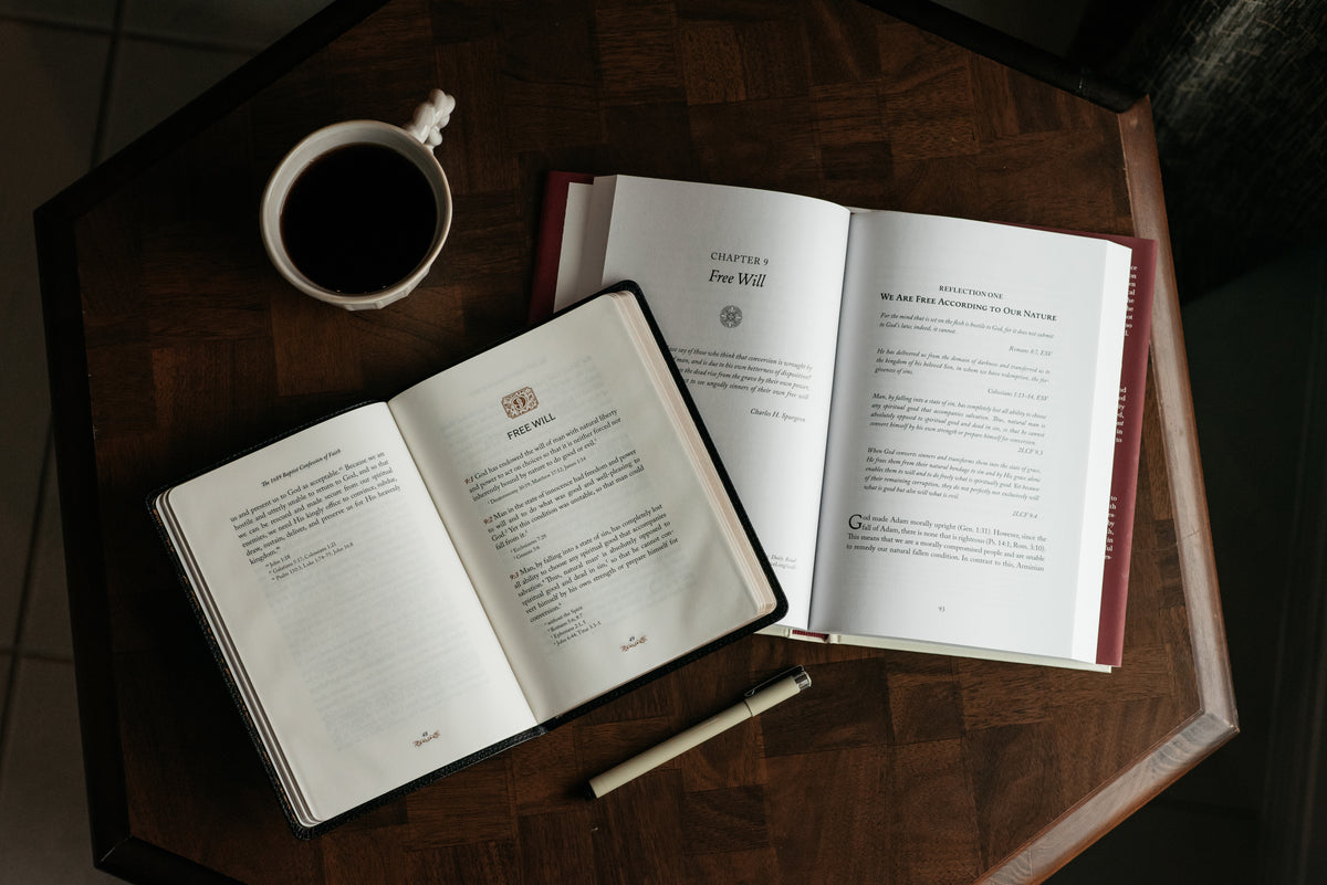 Two open books on a table with a pen and a cup of coffee. 