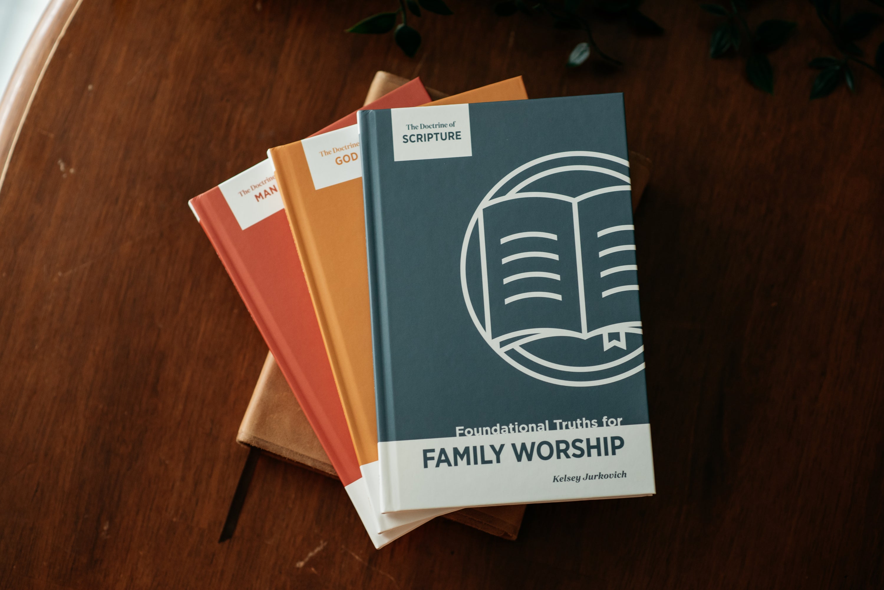 A stack of three books titled 'Foundational Truths for Family Worship' in different colors (teal, orange, coral) arranged on a dark wooden table.