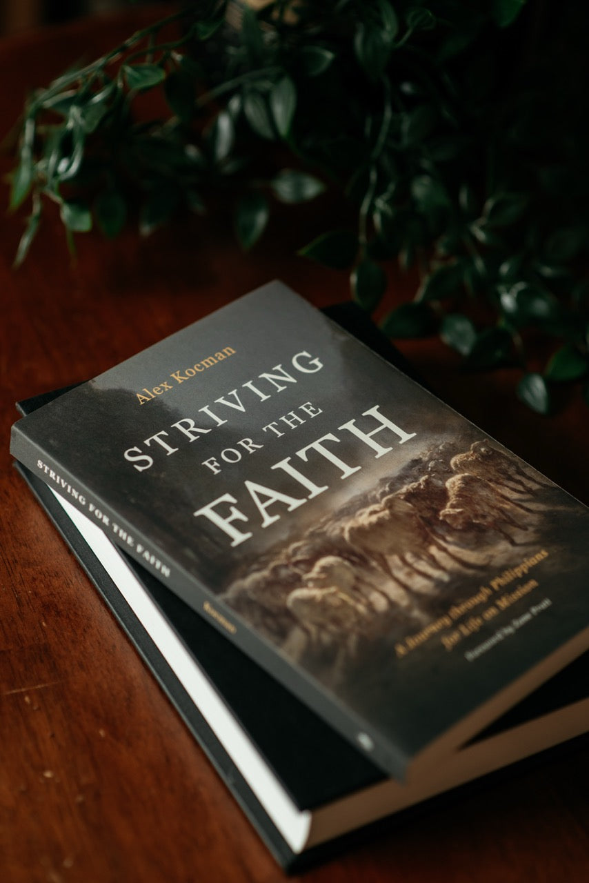 Striving for the Faith book on wood table with plant and notebook