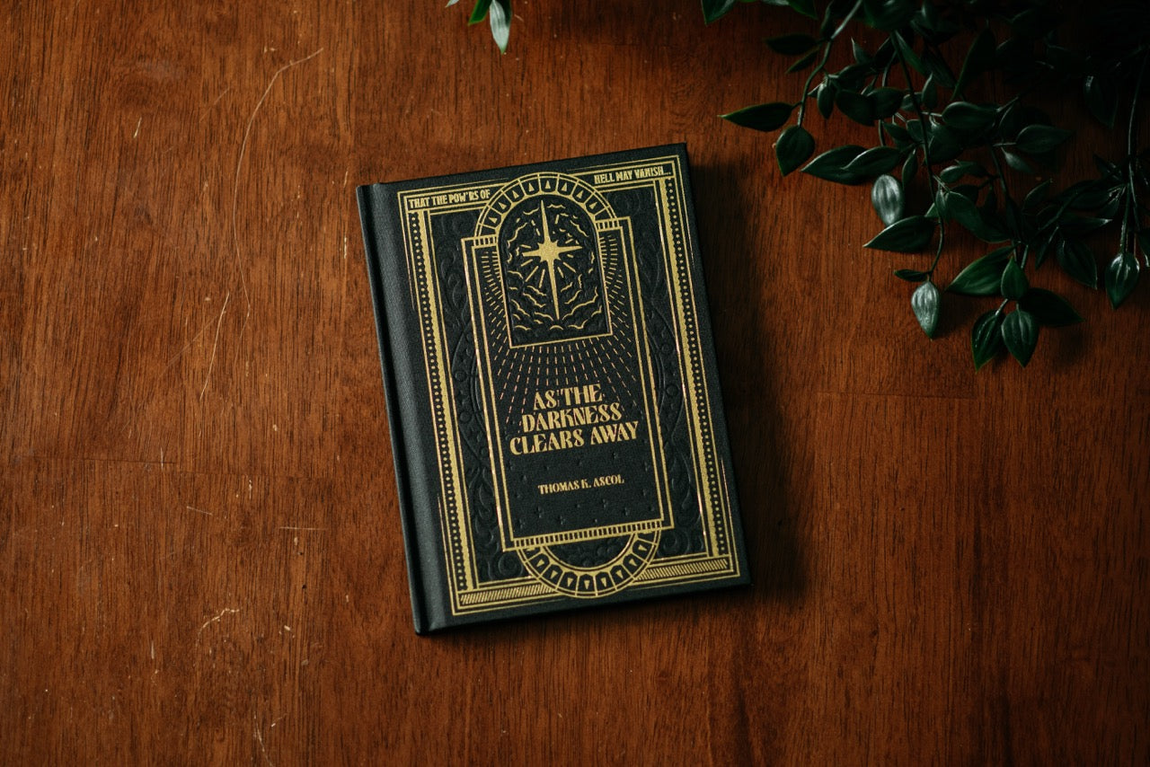 As the Darkness Clears Away book on wooden table with plant. 