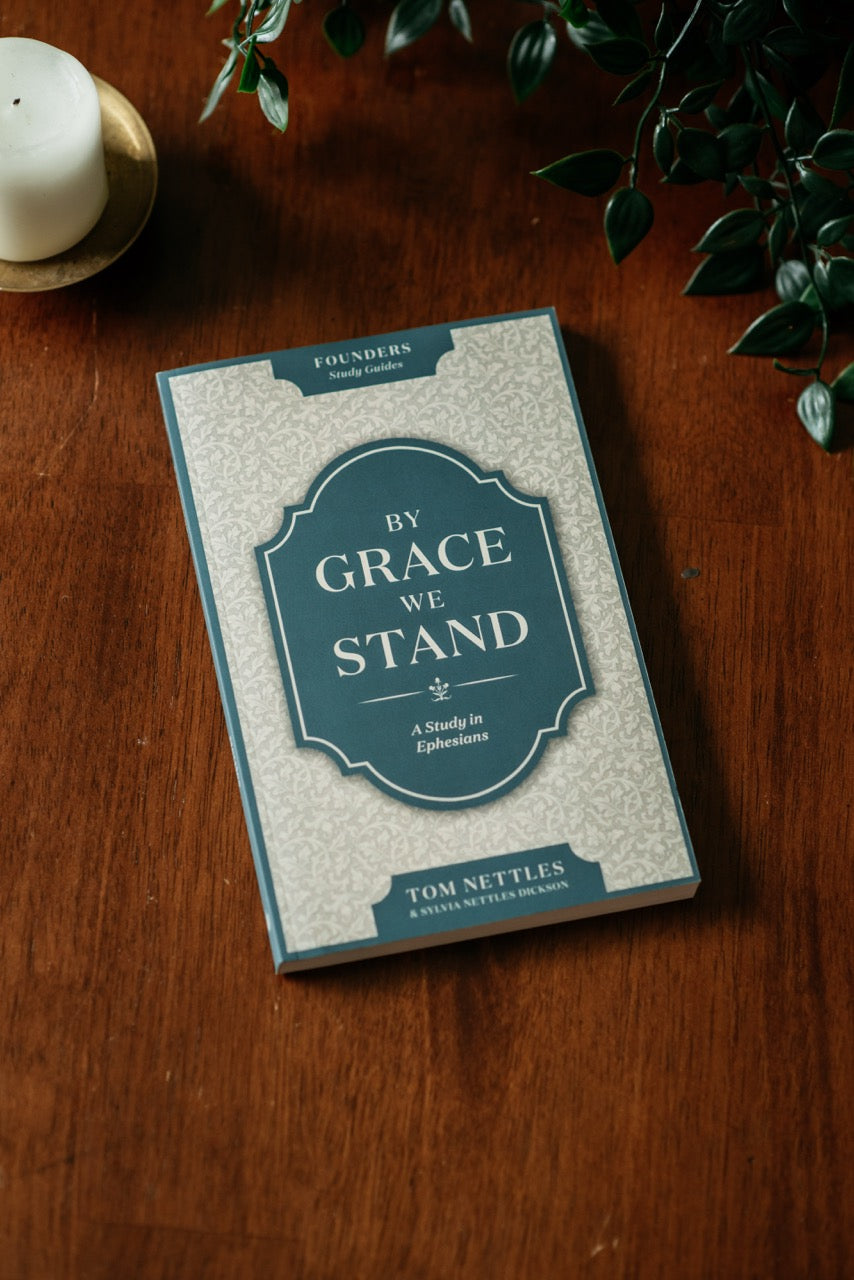 By Grace We Stand Book on wood table with plant and candle. 