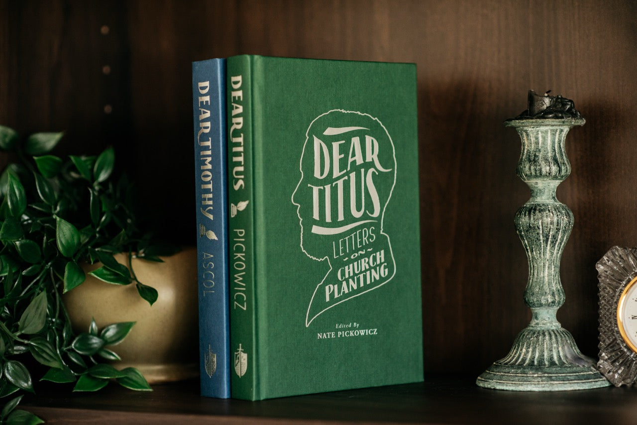 Dear Timothy and Dear Titus books on wood shelf with plant and decorative elements. 