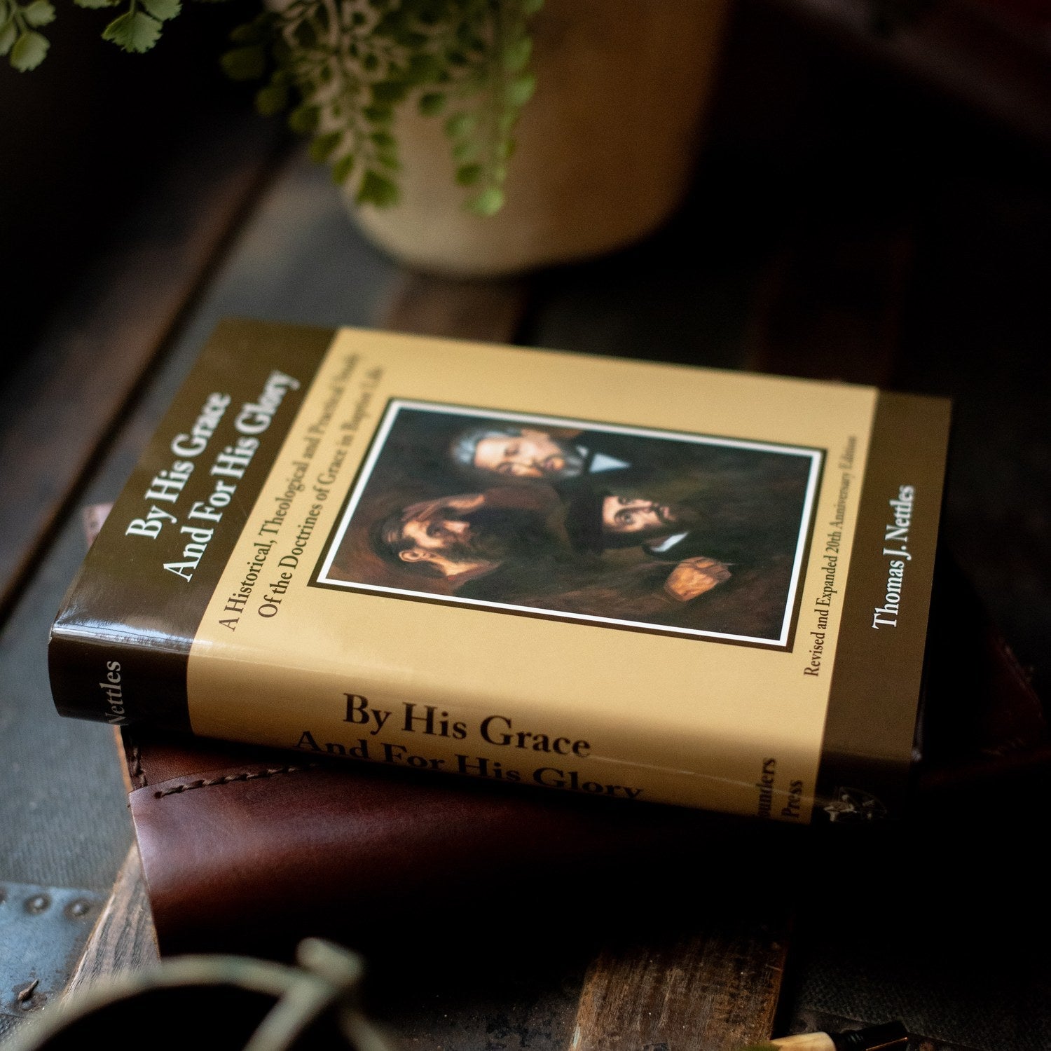 Book titled 'By His Grace And For His Glory' on a wooden surface with a plant in the background.