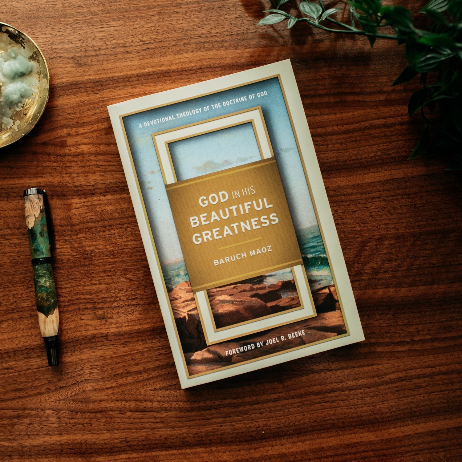 Book titled 'God in His Beautiful Greatness' by Baruch Maoz on a wooden surface with a pen and decorative items.