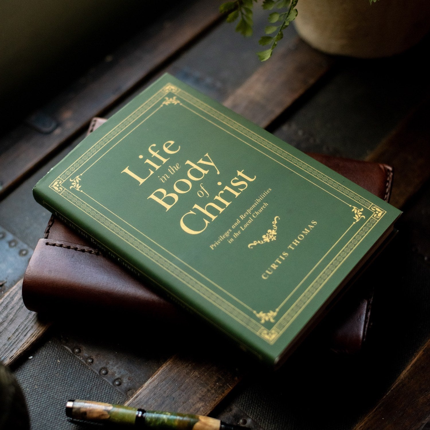 Green book titled 'Life in the Body of Christ' on a wooden surface