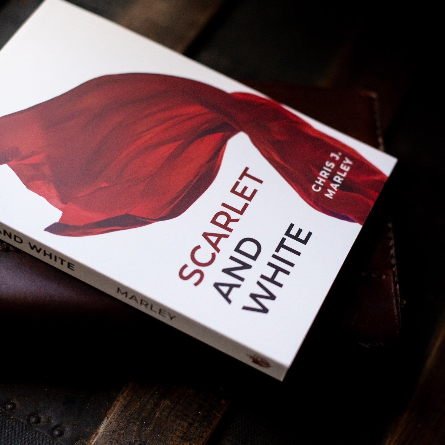 Book titled 'Scarlet and White' by Chris J. Marley on a dark surface