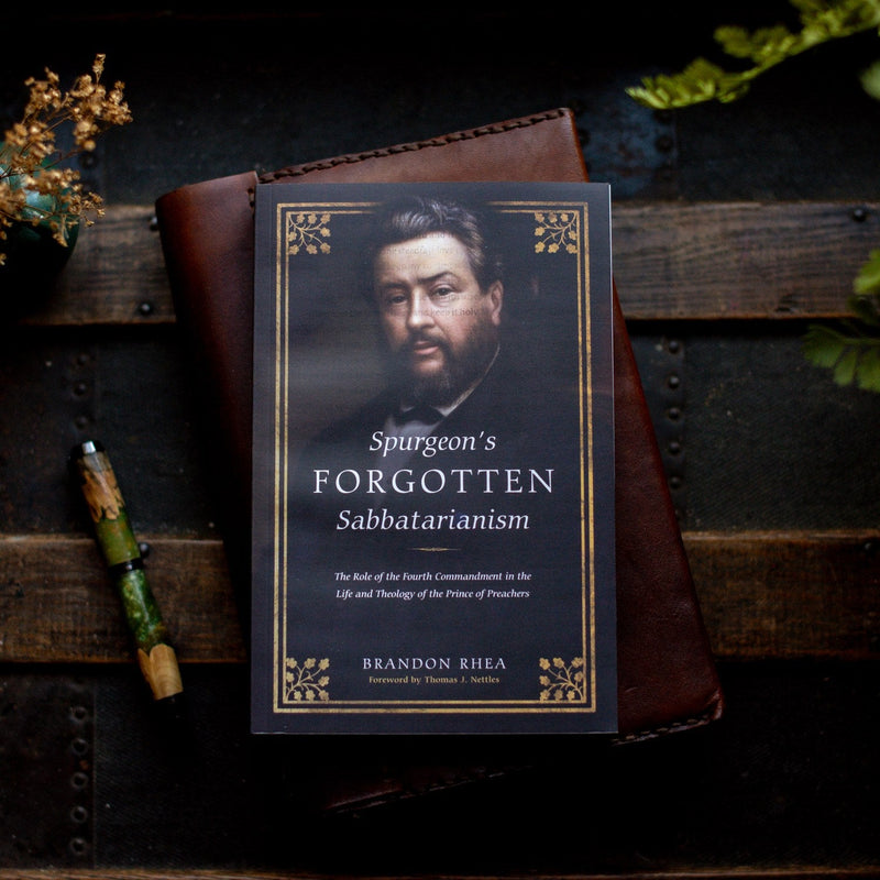 Book titled 'Spurgeon's Forgotten Sabattarianism' by Brandon Rhea on a wooden surface with a pen and decorative elements.