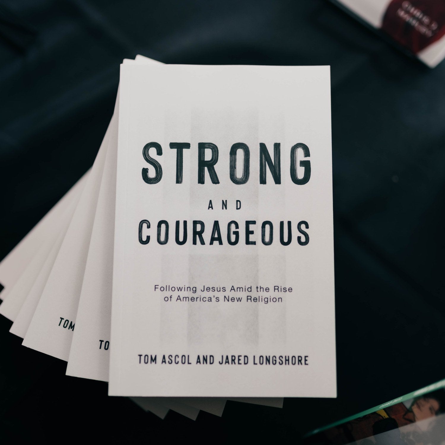 Stack of books titled 'Strong and Courageous' on a dark surface