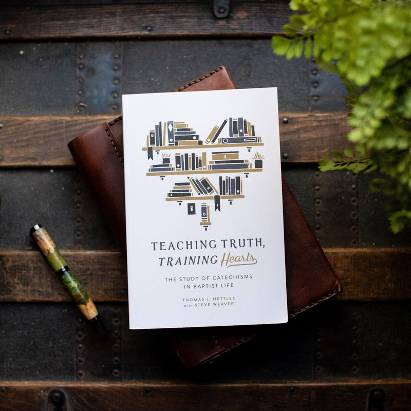 Booklet titled 'Teaching Truth, Training Hearts' on a wooden surface with a pen and plant.