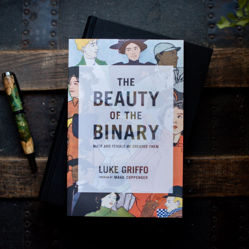 Book titled 'The Beauty of the Binary' by Luke Griffo on a wooden surface with a pen.